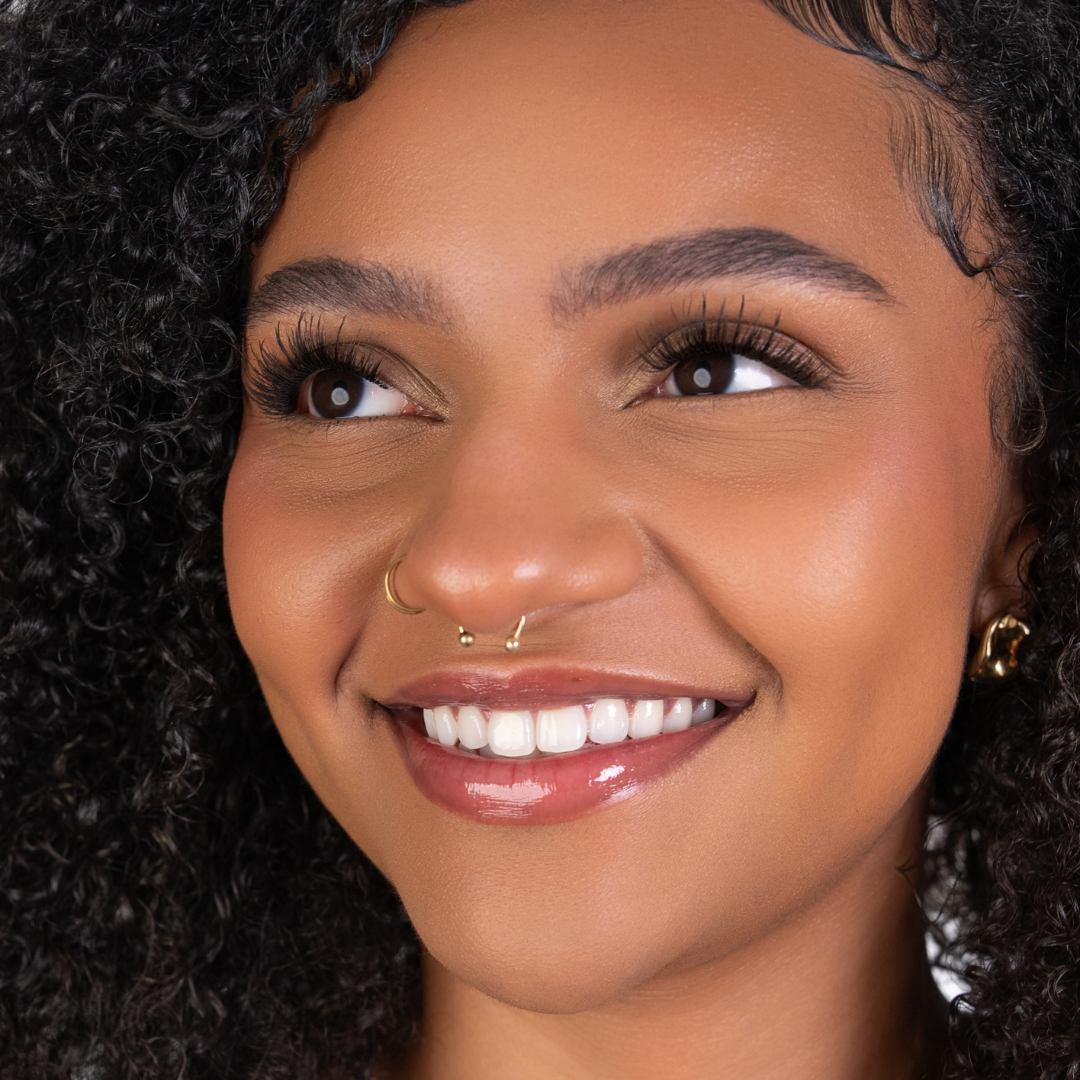 Close-up of a woman with a nose ring and earrings against a dark background